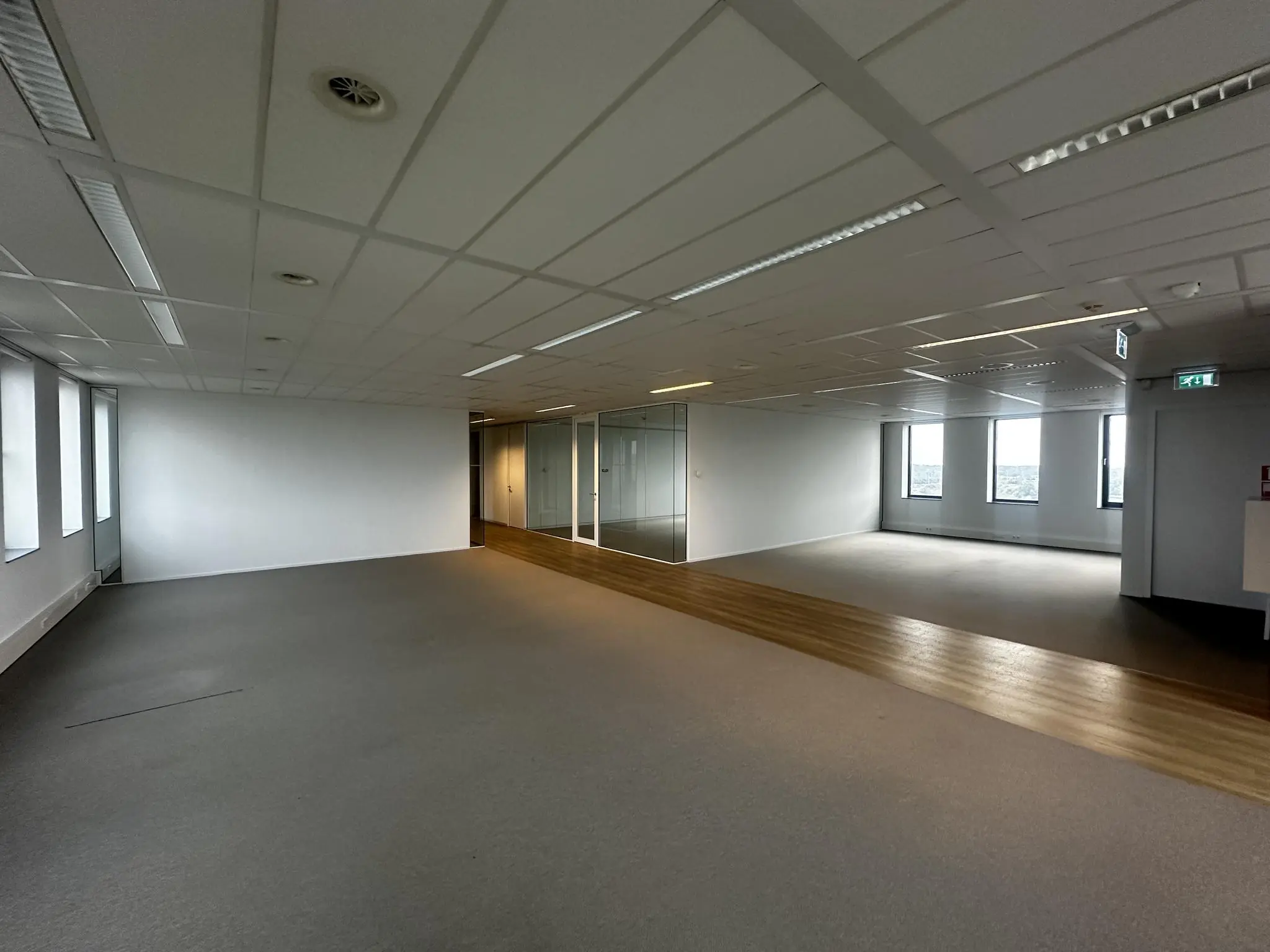 Leeg kantoorpand aan de Laan van Zuid Hoorn met tapijtvloer, houten looppad en glazen vergaderruimtes.